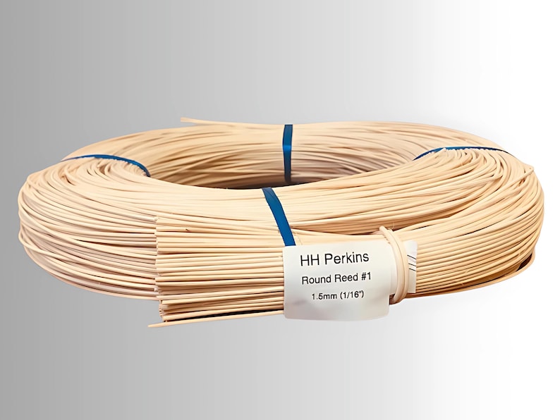 May include: A coil of natural-colored round reed, secured with blue bands. A label reads "HH Perkins Round Reed #1 1.5mm (1/16")". The reed is tightly wound, suggesting its use in weaving or crafting projects.