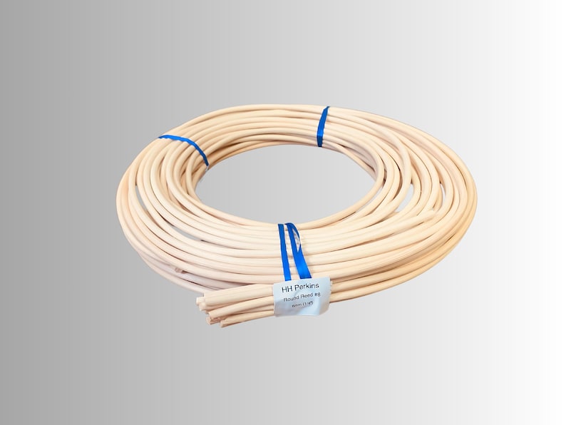 May include: A coiled bundle of light beige round reed, secured with blue ribbon. A white label with black text reads "HH Perkins Round Reed #8 6mm (1/4")". The reed is a natural color, suitable for crafting and weaving projects.