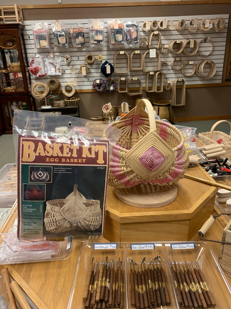 May include: A basket weaving kit for making an egg basket. The kit includes natural colored reeds and instructions. The kit is packaged in a clear plastic bag with a pink and white woven basket on display.