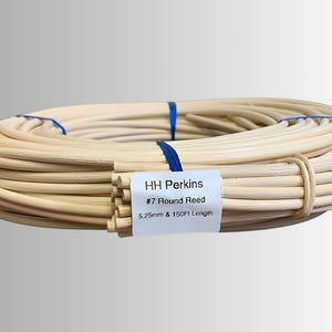 May include: A coiled bundle of natural-colored round reeds, secured with blue ribbon and a tan band. A white label reads "HH Perkins #7 Round Reed 5.25mm & 150Ft Length". The reeds are tightly wound, suggesting a craft or DIY project.