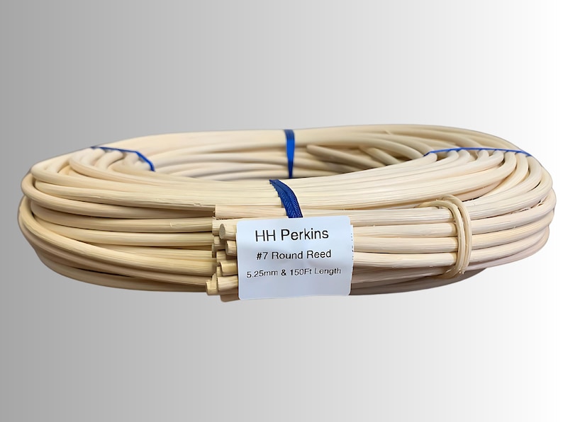 May include: A coiled bundle of natural-colored round reeds, secured with blue ribbon and a tan band. A white label reads "HH Perkins #7 Round Reed 5.25mm & 150Ft Length". The reeds are tightly wound, suggesting a craft or DIY project.