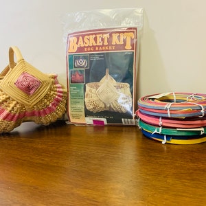 May include: A wicker egg basket kit with a finished basket, instructions, and colorful reeds. The basket is woven with pink and natural colored reeds.
