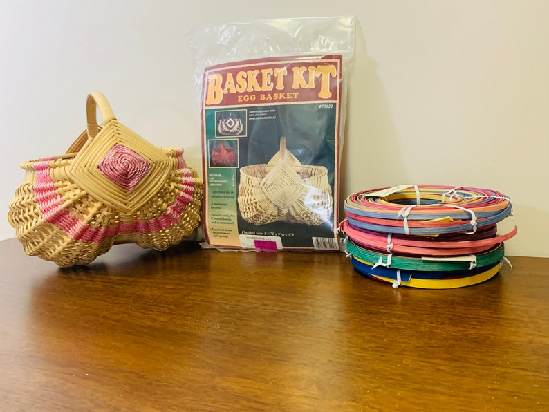 May include: A wicker egg basket kit with a finished basket, instructions, and colorful reeds. The basket is woven with pink and natural colored reeds.