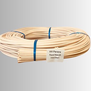 May include: A bundle of natural-colored round reed, tightly coiled and secured with blue bands. A smaller bundle of reeds is visible, with a label that reads "HH Porkins Round Reed #5 3.5mm (9/64)".