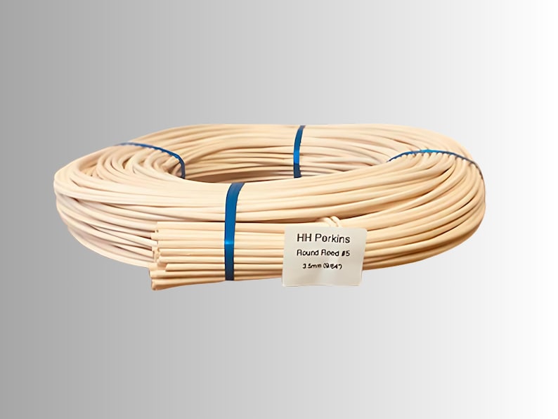 May include: A bundle of natural-colored round reed, tightly coiled and secured with blue bands. A smaller bundle of reeds is visible, with a label that reads "HH Porkins Round Reed #5 3.5mm (9/64)".