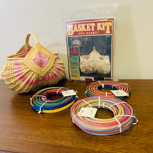 May include: A wicker egg basket kit with instructions and colorful reeds for weaving. The basket is pink and white with a diamond pattern. The reeds are in three bundles, each with a different color combination.