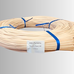 May include: A coiled bundle of light-colored round reed, secured with blue ribbon. A white label displays the text "HH Perkins Round Reed #2 1.75mm". This reed is likely used for weaving or crafting projects.
