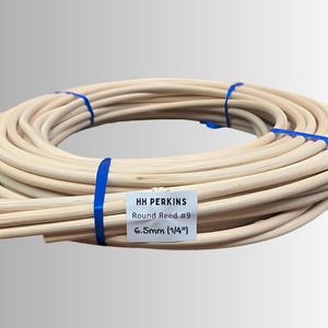 May include: A coiled bundle of light-colored round reeds, secured with blue bands. A white label indicates the product is "HH PERKINS Round Reed #9" with a diameter of 6.5mm (1/4"). The reeds are tightly wound, suggesting a craft or DIY project.