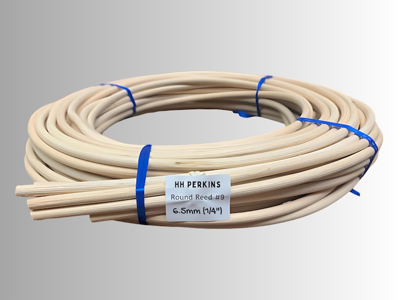 May include: A coiled bundle of light-colored round reeds, secured with blue bands. A white label indicates the product is "HH PERKINS Round Reed #9" with a diameter of 6.5mm (1/4"). The reeds are tightly wound, suggesting a craft or DIY project.