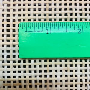 May include: Close-up of a woven rattan material with a green ruler across the top. The ruler, marked in inches, reads "MADE IN USA". The rattan has a light beige color and a square grid pattern.