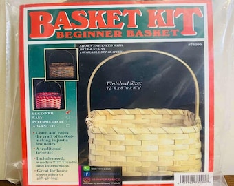 May include: A beginner basket kit in a clear plastic package. The packaging features the text BASKET KIT BEGINNER BASKET and shows a woven light-colored reed basket with a wooden D-handle. The finished size is listed as 12 inches h x 8 inches w x 8 inches d.