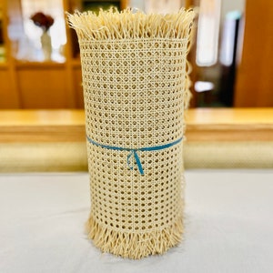 May include: A roll of natural cane webbing with a fringed edge. The webbing is tied with a blue ribbon.