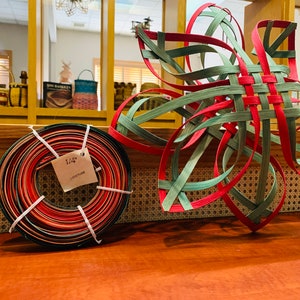 May include: A coil of 1/4 inch wide, multi-colored, woven reed, and a red and green woven star-shaped craft project.