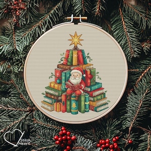 May include: A cross-stitch embroidery hoop depicting a Christmas tree formed from books. Santa Claus, dressed in red, is reading a book. The tree is topped with a gold star. The background is a neutral colour, and the hoop is surrounded by evergreen branches.