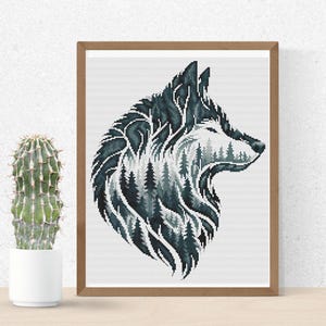 Puede incluir: Una obra de arte en punto de cruz enmarcada que representa la cabeza de un lobo. El lobo está representado en tonos de verde azulado y gris, con una escena de bosque en su interior. La obra se presenta en un marco de madera.