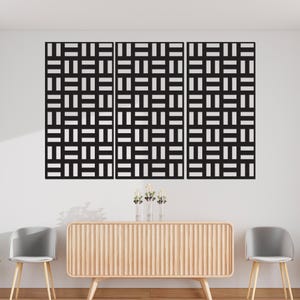 Könnte beinhalten: Drei schwarze geometrische Wandpaneele mit einem gewebten Muster. Die Paneele sind horizontal angeordnet und an einer weißen Wand montiert.