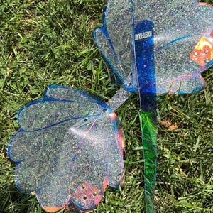 May include: A pair of translucent blue acrylic wings featuring a dense silver glitter finish and scalloped edges. The wings are connected by a central vertical spine that displays the text HOUSEOFPOLARIS in white lettering, with small metal rivets.