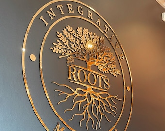 Może przedstawiać: Okrągły znak w kolorze złotym z napisem "Integrative Roots Medicine" i stylizowanym drzewem z korzeniami. Znak jest zamontowany na ciemnoszarej ścianie, pod którym znajduje się półka. Na półce stoją cztery małe doniczki z roślinami.