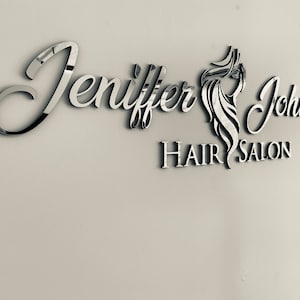 K&ouml;nnte beinhalten: Ein silbernes Schild mit dem Text "Jennifer Johnson Hair Salon" in einer kursivschriftlichen Schriftart. Das Schild zeigt ein stilisiertes Bild von Frauenhaaren.