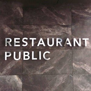 K&ouml;nnte beinhalten: Ein Schild an einer Wand mit der Aufschrift "RESTAURANT PUBLIC" in silbernen Buchstaben.