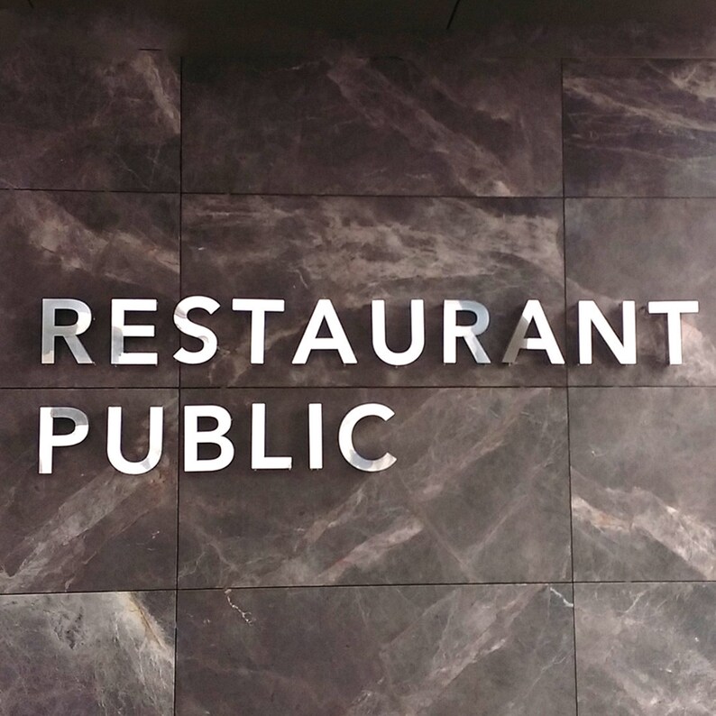 K&ouml;nnte beinhalten: Ein Schild an einer Wand mit der Aufschrift "RESTAURANT PUBLIC" in silbernen Buchstaben.