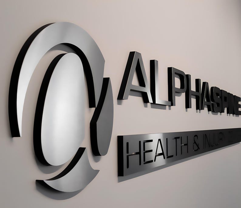 K&ouml;nnte beinhalten: Ein silbernes und schwarzes 3D-Schild mit dem Text "ALPHASPIRE HEALTH & INDUSTRIES" an einer wei&szlig;en Wand.