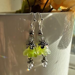 May include: A pair of dangle earrings featuring lime green flower-shaped beads topped with silver-toned metal caps. Each earring includes clear faceted crystal beads, silver-toned spacer beads, and a silver-toned hook wire for attachment.