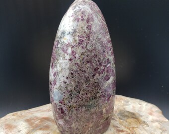 May include: A polished, freeform, pink and white, ruby in fuchsite crystal point. The crystal has a smooth, rounded shape and a speckled appearance.