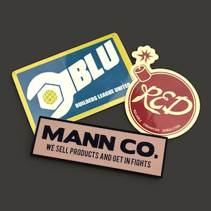 May include: Three rectangular and circular stickers featuring logos. One blue rectangular sticker reads BLU BUILDERS LEAGUE UNITED. One red circular sticker shows a bomb icon and reads RED RELIABLE EXCAVATION DEMOLITION. One beige rectangular sticker reads MANN CO. WE SELL PRODUCTS AND GET IN FIGHTS.