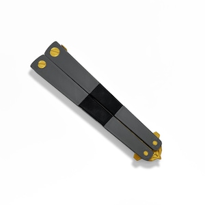 Angled three-quarter view of closed TF2 Spy Butterfly Knife replica showing smoky black balisong handles with brass pivot screws, Team Fortress 2 cosplay prop