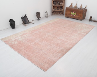 May include: A light pink vintage rug with a faded floral pattern. The rug has a distressed look and is made of natural fibers.