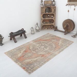 May include: A vintage-style rug with a faded, cream-coloured background and a central design in shades of peach, grey, and brown. The rug has a distressed, worn look, adding to its charm.