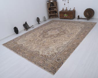 May include: Large, rectangular, beige and brown patterned rug. The rug features an intricate floral design with a central medallion and a detailed border. The rug is placed on a white floor, with other decorative items in the background.