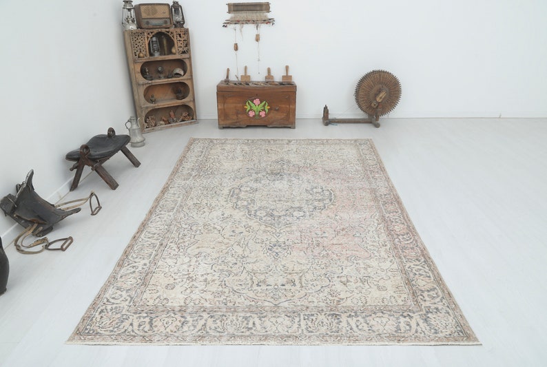 May include: A vintage-style rug with a cream background and a faded floral pattern in shades of gray, pink, and brown. The rug has a decorative border.