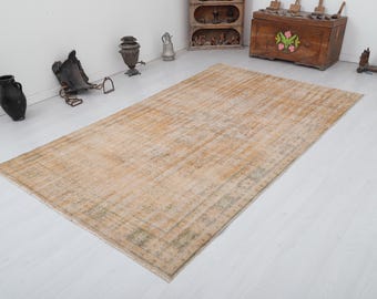 Può includere: Un tappeto in stile vintage dall'aspetto sbiadito e usurato. Il tappeto ha uno sfondo beige chiaro con un sottile motivo di linee verdi e marroni. È un tappeto rettangolare con un bordo a frange.