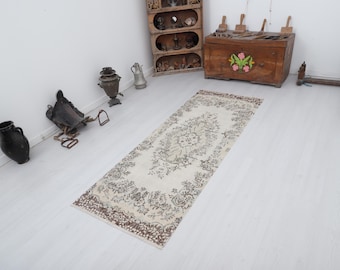 May include: A rectangular, vintage-style rug with a cream-colored background and a detailed floral pattern in shades of brown and gray. The rug has a decorative border and is placed on a white wooden floor.