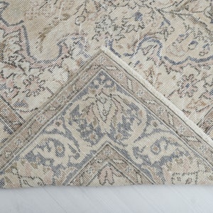 May include: A close-up of a beige and gray patterned rug with a fringed edge. The rug has a floral design and is folded in half.
