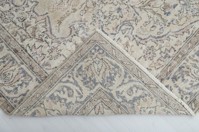May include: A close-up of a beige and gray patterned rug with a fringed edge. The rug has a floral design and is folded in half.