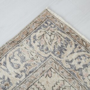 May include: Close-up of a corner of a beige and gray patterned rug with a fringe border.