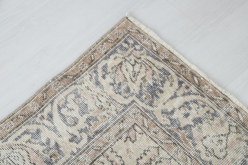 May include: Close-up of a corner of a beige and gray patterned rug with a fringe border.