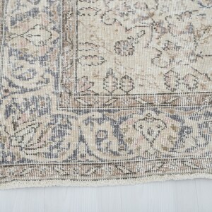 May include: Close-up of the bottom edge of a vintage rug with a faded floral pattern in shades of beige, brown, and blue.