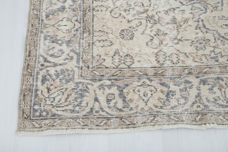 May include: Close-up of the bottom edge of a vintage rug with a faded floral pattern in shades of beige, brown, and blue.