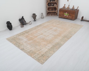 Può includere: Un tappeto vintage beige chiaro con un motivo floreale verde sbiadito attorno al bordo. Il tappeto è steso su un pavimento bianco.