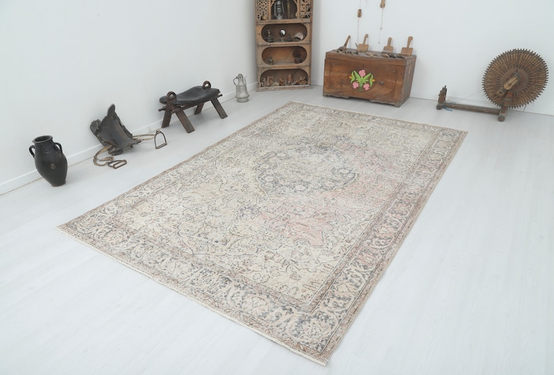 May include: A vintage rug with a cream background and a faded floral pattern in shades of pink, gray, and brown. The rug has a distressed look and is perfect for adding a touch of vintage charm to any room.