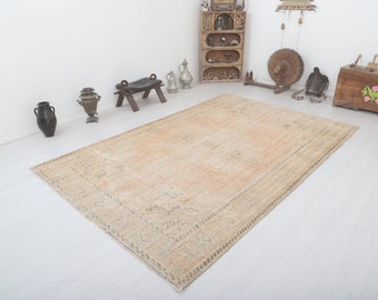 May include: A light beige vintage rug with a faded floral pattern and a dark brown border. The rug is laid out on a white floor.