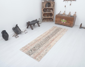 May include: A rectangular, vintage-style rug with a central patterned stripe in shades of brown, beige, and red. The rug is surrounded by lighter beige stripes. The rug is placed on a white floor.