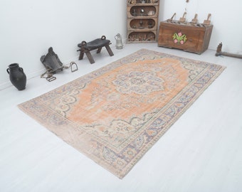 Pode incluir: Um tapete vintage tecido à mão com um fundo pêssego desbotado e padrões florais intrincados em tons de azul e creme. O tapete tem um aspecto desgastado e desbotado, o que aumenta o seu charme.