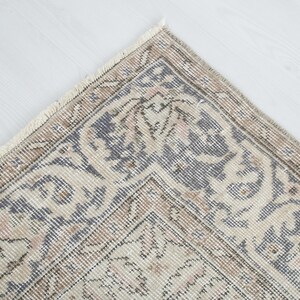 May include: Close-up of a corner of a vintage rug with a beige background and a blue and brown floral pattern. The rug has a fringe border.