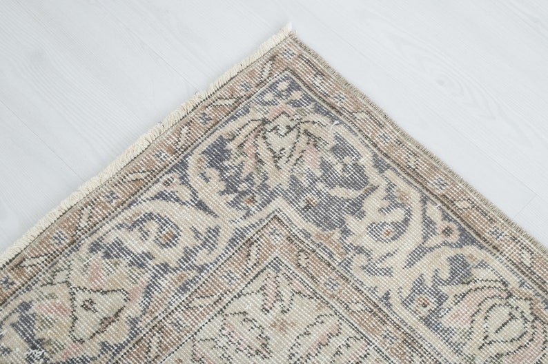 May include: Close-up of a corner of a vintage rug with a beige background and a blue and brown floral pattern. The rug has a fringe border.