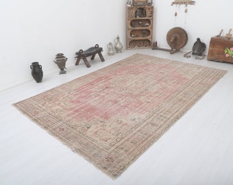 May include: A vintage rug with a faded pink and beige color scheme. The rug has a floral pattern and a border with intricate details. The rug is laid out on a white floor.